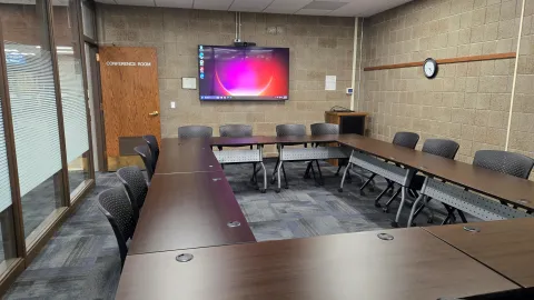 Conference Room with tables and chairs in a rectangular shape, TV on the wall.